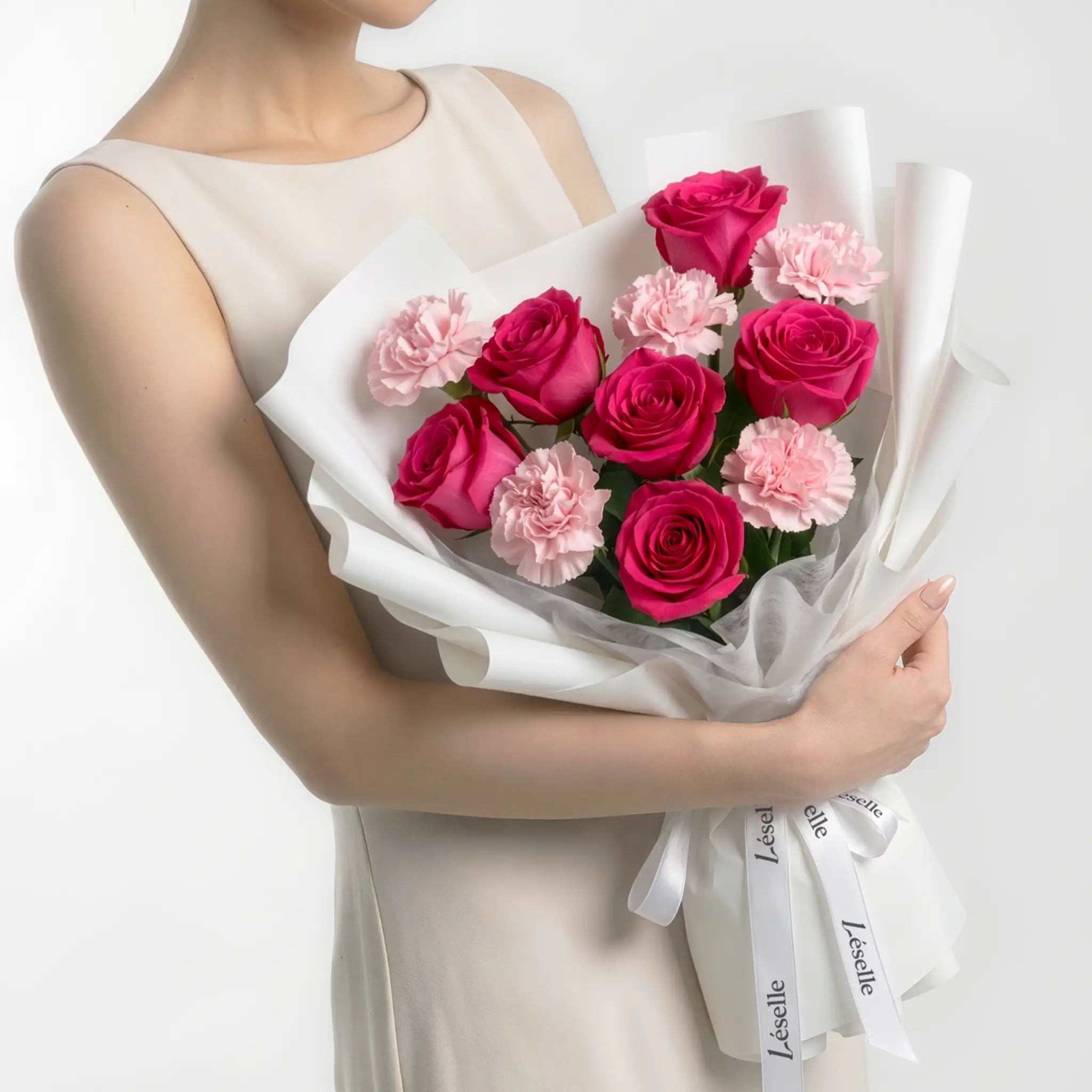 Bouquet of hot pink roses and blush carnations held by a person in a white dress on a white background